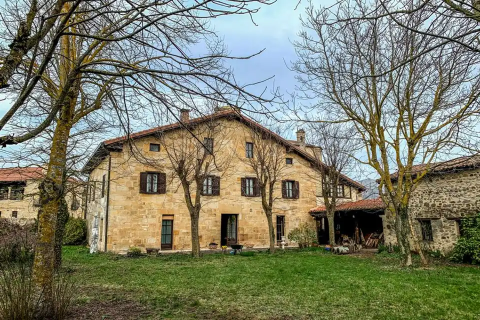 Grande maison en pierre sous un toit de tuiles, entourée d'arbres sans feuilles